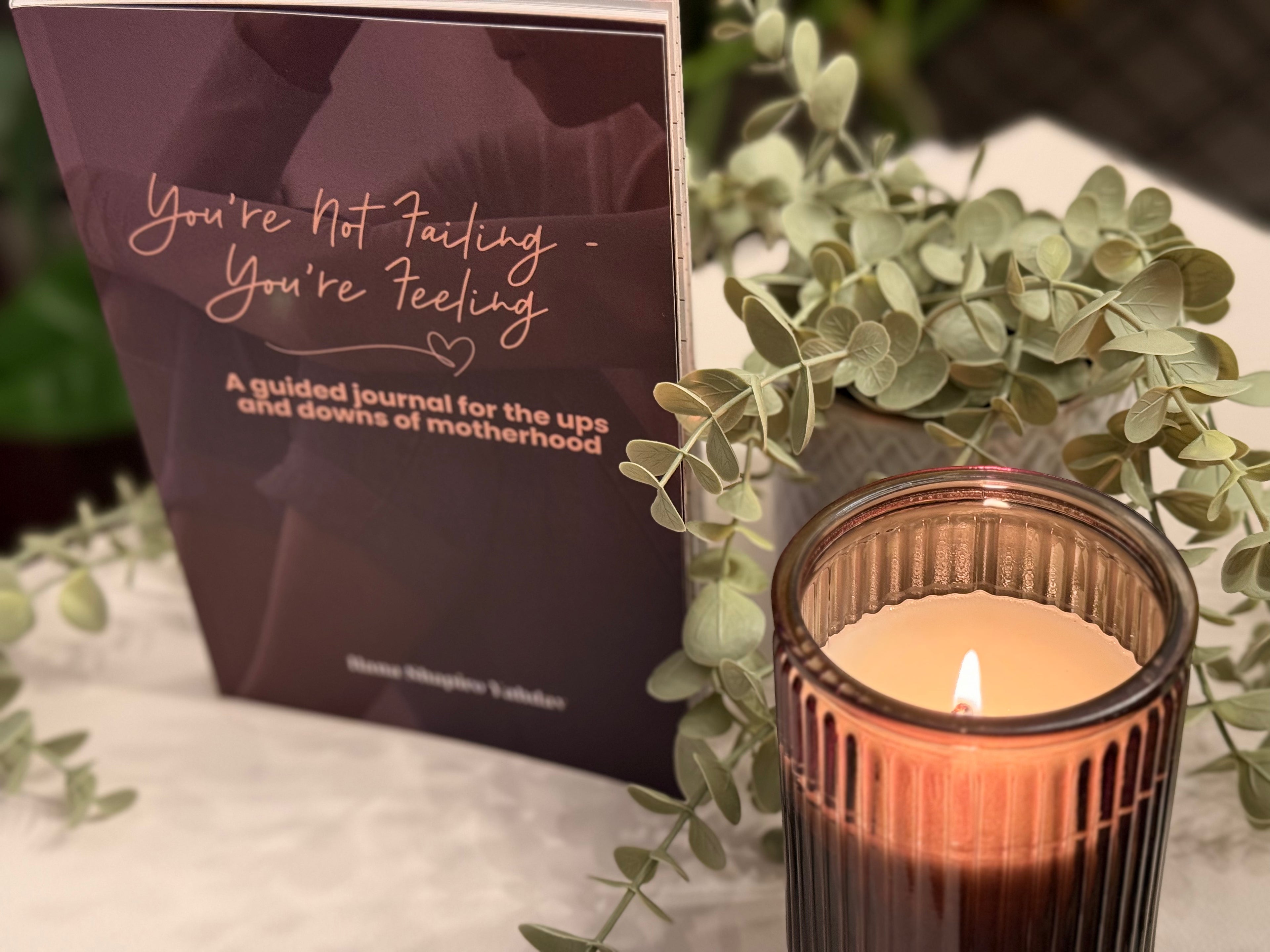 Guided journal for mothers with a lit candle and greenery on a surface
