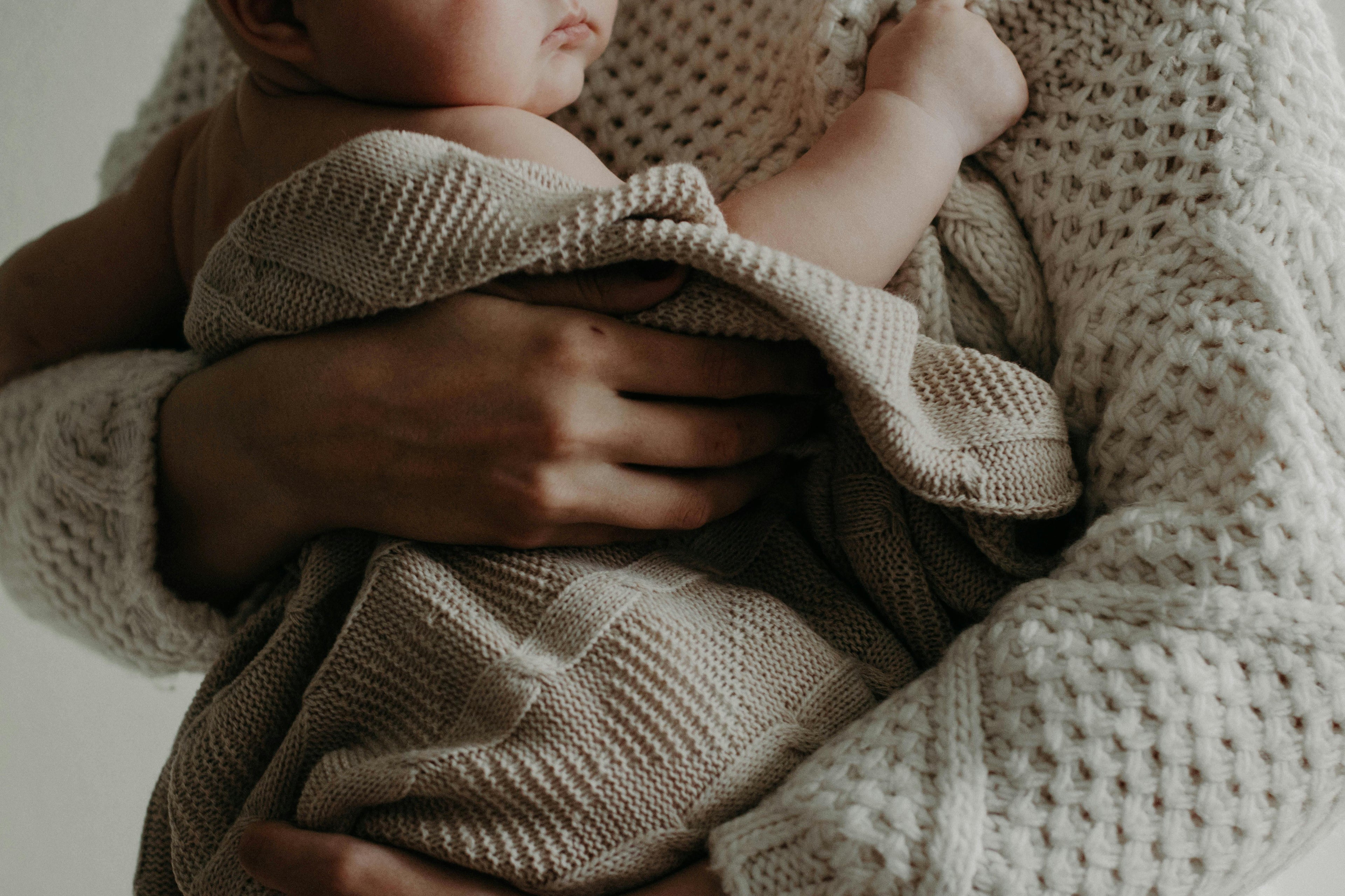 Person holding a baby wrapped in a beige knitted blanket